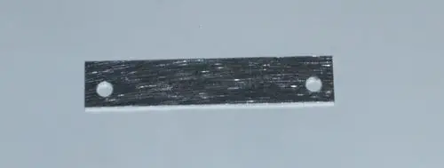 Metallstreifen mit zwei Löchern, möglicherweise zur Befestigung, auf einem hellen Hintergrund. Produkt könnte mit Daikin Altherma 3 R W in Verbindung stehen.